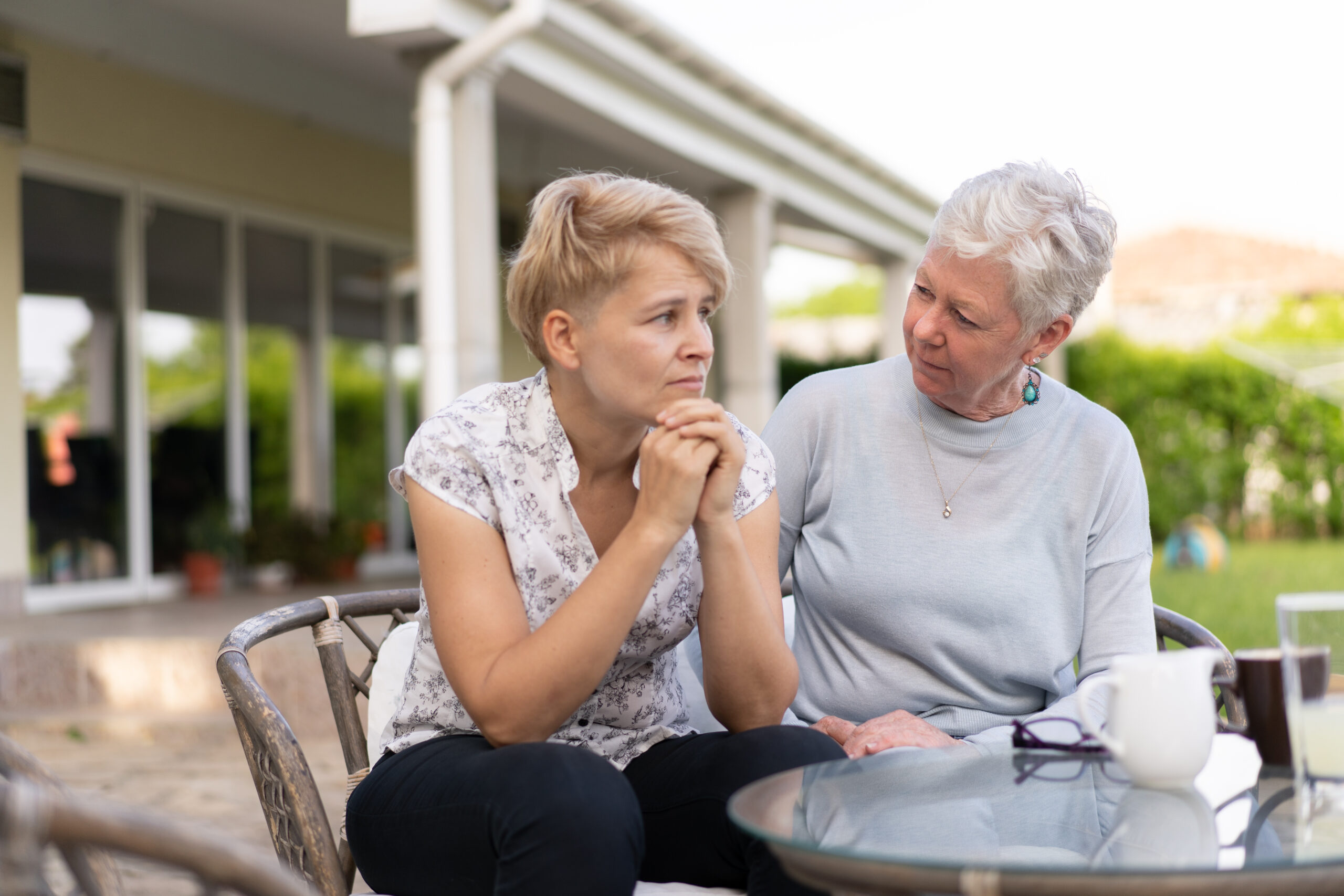 A sad grown-up woman is being soothed by her mother sitting next to her, the grey haired mother is concerned for her daughter
